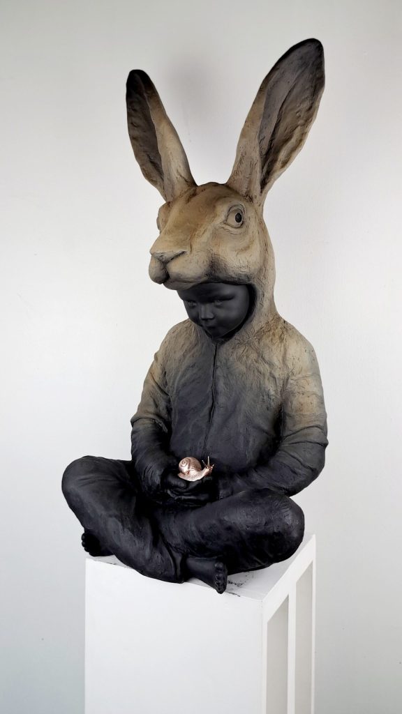 Hannes Verhoeven, "Slow Down," marble composite, 80 cm — child in a hare costume seated cross-legged holding a small gilded snail