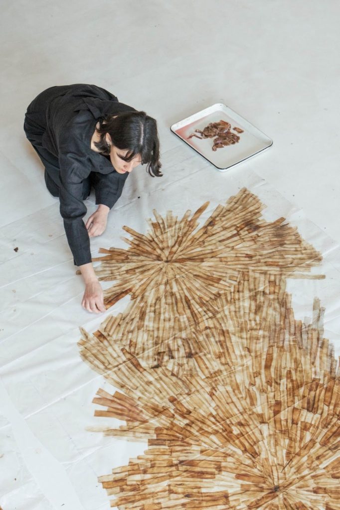 Loumi Le Floc'h kneeling on the studio floor, assembling a radial, fan-shaped Precious Peels panel